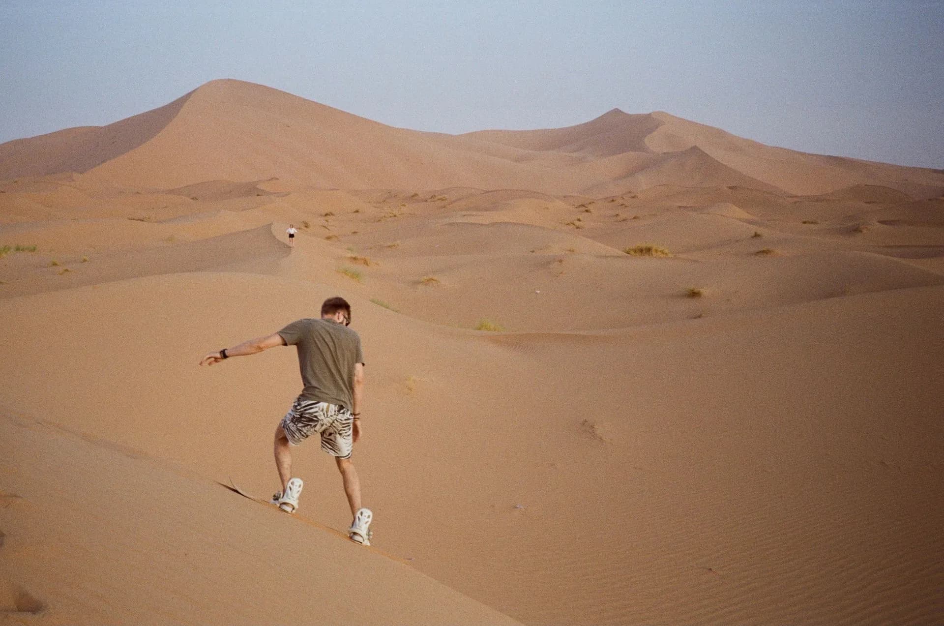 Sandboarder riding down a large dune in the Chilca desert south of Lima, Peru, with a 4x4 parked at the ridge