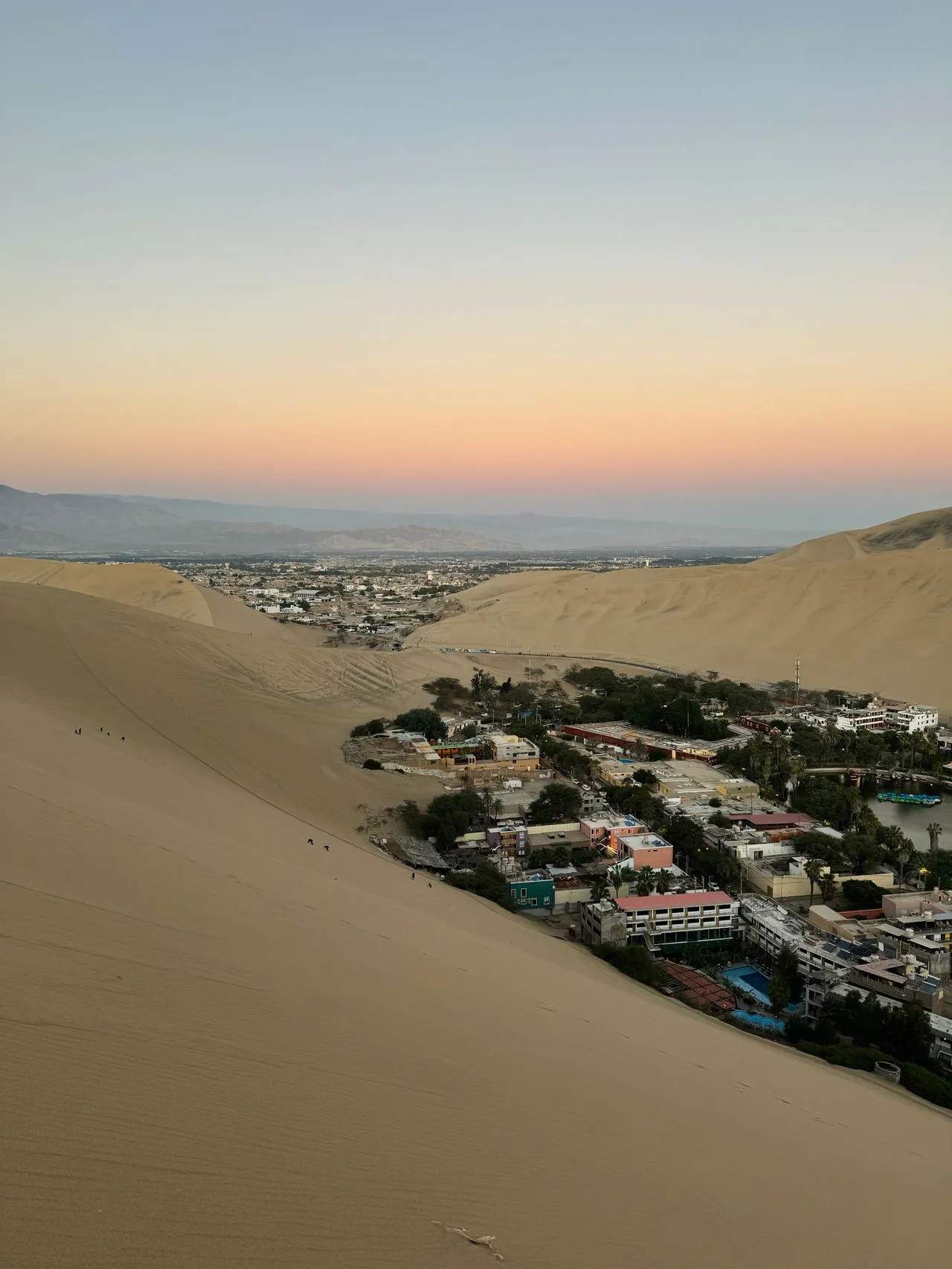 The Huacachina oasis lagoon and palm trees ringed by desert dunes at sunset in Peru