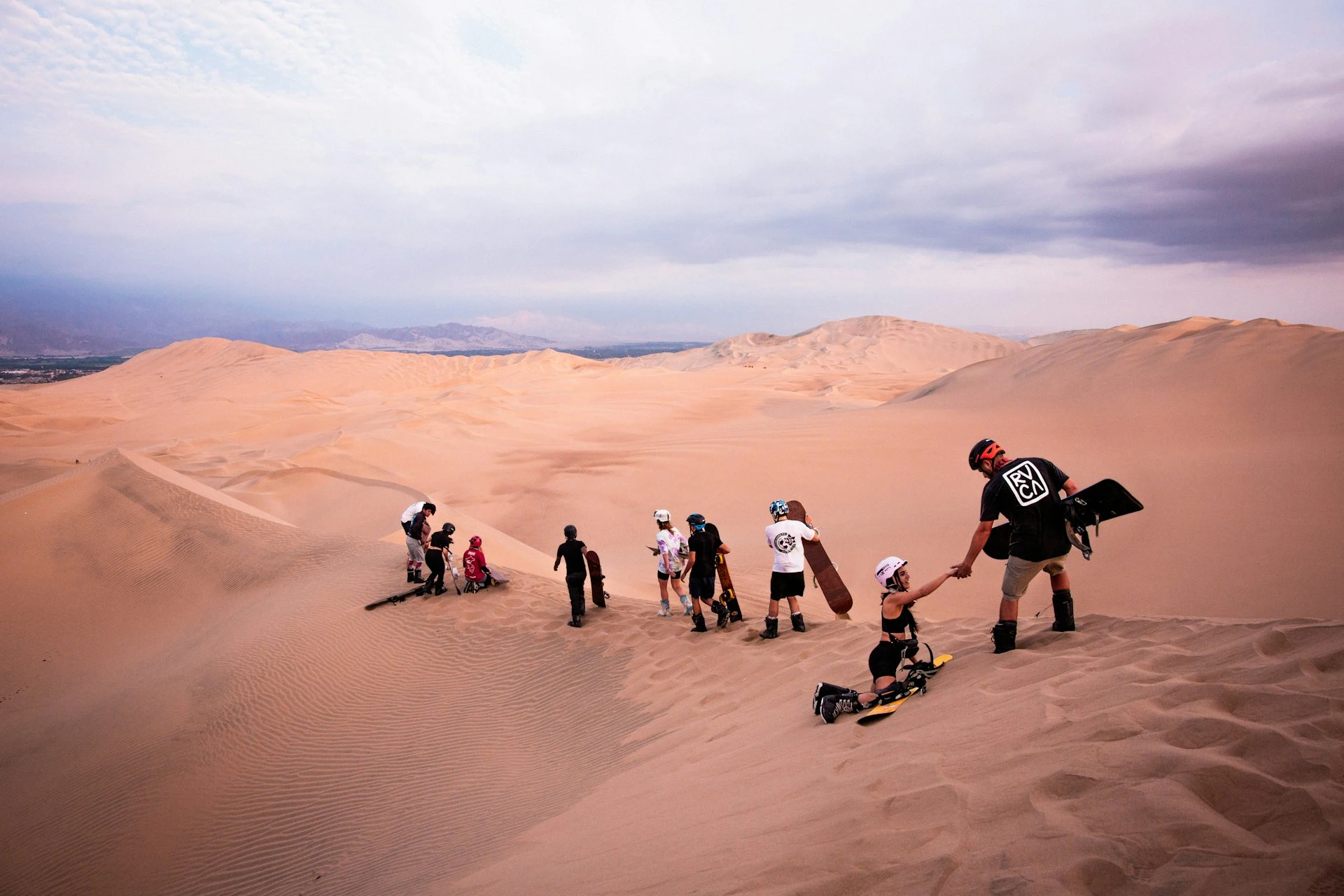 Sandboarders lined up at the top of a dune above the Huacachina oasis in Peru